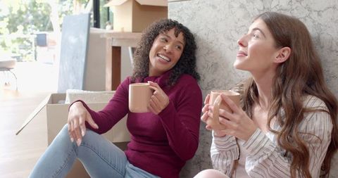 Two happy friends relaxing with hot drinks during moving day