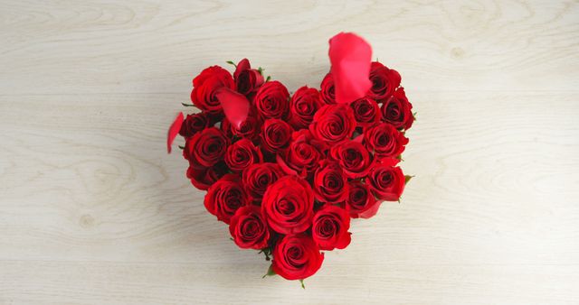 Heart-shaped arrangement of vibrant red roses on light wooden surface. Perfect for celebrating romantic occasions such as Valentine's Day or anniversaries. Great for use in advertising, greeting cards, or as decorative imagery for websites and social media.