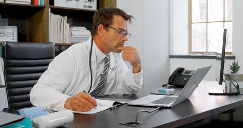 Focused Middle-Aged Doctor Analyzing Patient Information on Laptop