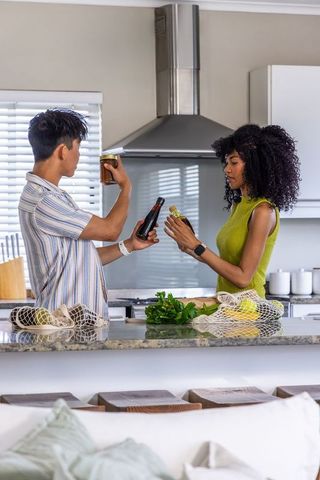 Diverse couple comparing condiments and produce on kitchen island with lemons and herbs