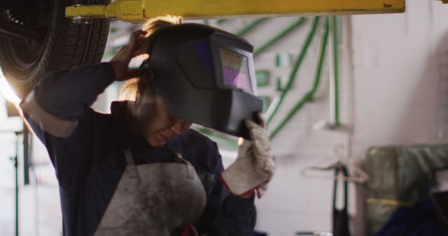 Portrait of female mechanic wearing welding helmet under a car at a car service station. automobile repair service concept