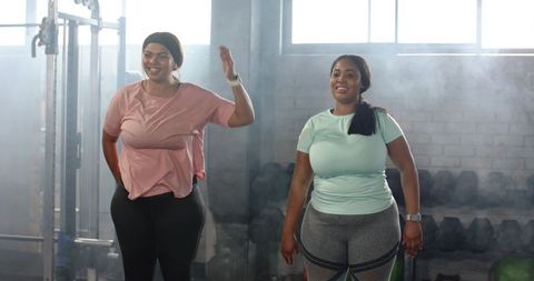 African american women training together in gym smiling and raising arms wearing smartwatch