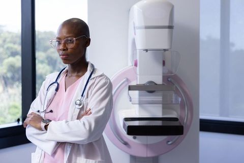 African female radiographer standing beside mammography machine wearing pink scrubs