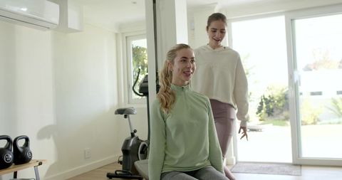 Female friends training together in bright home gym smiling during strength workout