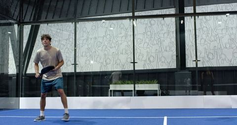 Focused male padel player in action on modern blue court