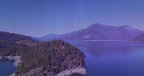 Jutting forested peninsula extending into calm alpine lake with mountain reflections