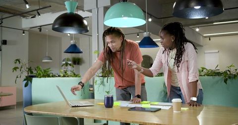 African american coworkers collaborating over laptop in modern pastel coworking space