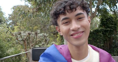 Smiling young man draping rainbow flag in serene garden setting