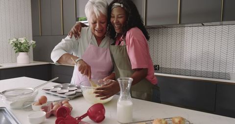 Grandmother and Granddaughter Mixing Batter and Laughing in Modern Kitchen