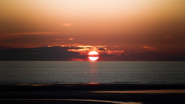 Sun setting over a tranquil ocean with a fiery red sky creates a serene and picturesque scene. Ideal for use in travel promotions, nature blogs, relaxation or mindfulness content, and as a desktop wallpaper to evoke calm and beauty.
