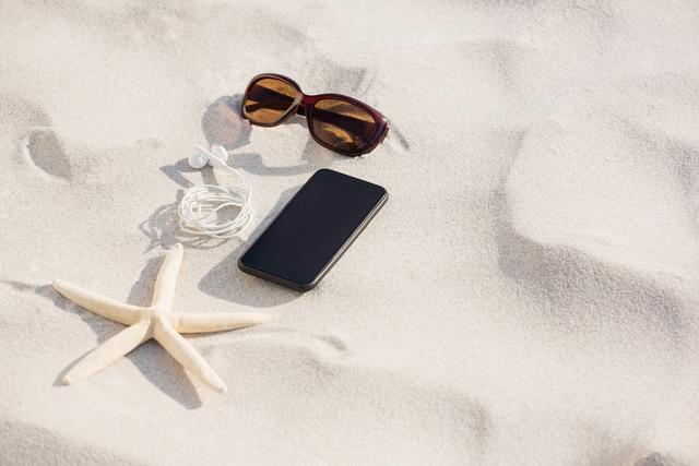 Starfish, sunglasses, headphones and mobile phone kept on sand - Download Free Stock Photos Pikwizard.com