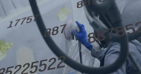 African american auto body technician sanding vehicle panel in spray booth with respirator