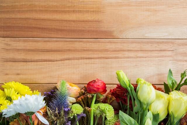 This image features a variety of colorful flowers arranged against a wooden background. Ideal for use in spring or summer-themed designs, gardening blogs, floral shop advertisements, or as a decorative element in invitations and greeting cards.