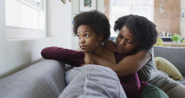 Sad african american mother and daughter sitting on sofa, embracing. domestic life and quality family time together at home.