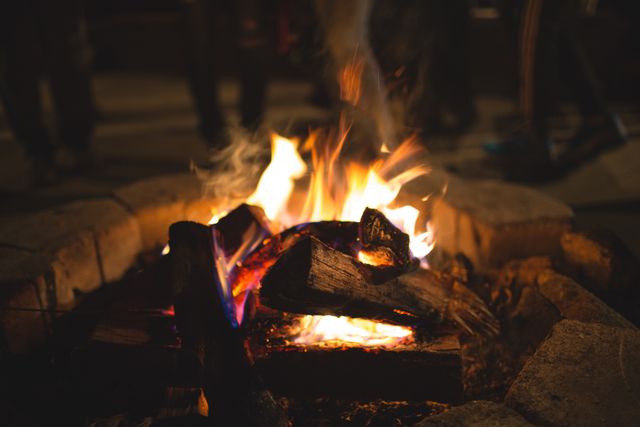 A warm campfire with burning logs during night time. Ideal for illustrating outdoor activities, camping trips, and cozy gatherings.