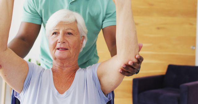 Senior woman receiving physical therapy assistance, lifting arms with help of caregiver. Ideal for topics on elderly care, rehabilitation, physiotherapy, health and wellness, and support for seniors.