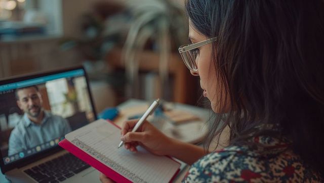 Young woman in home office taking notes during online meeting