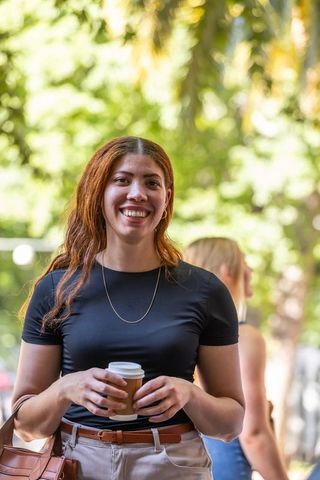 Smiling african american woman holding takeaway coffee in sunlit urban park walkway