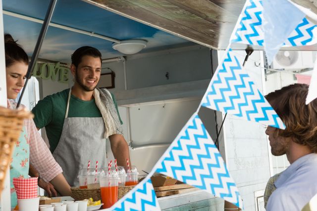 Smiling vendor serving a customer at a food truck, with beverages and snacks visible. Ideal for use in articles about street food culture, small businesses, and outdoor events. Perfect for marketing materials for food festivals, urban markets, and casual dining experiences.