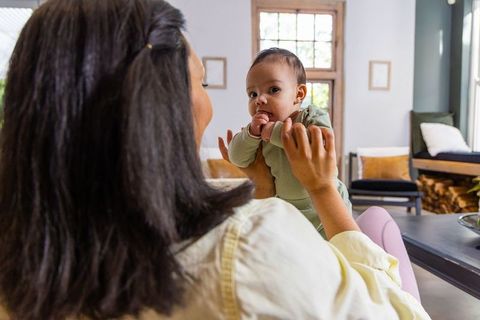 Mother holding newborn on couch in cozy modern living room with natural light