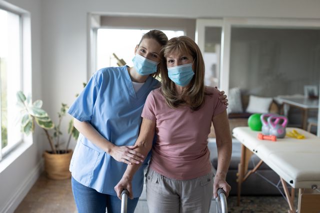 Portrait of Senior Caucasian woman at home visited by Caucasian female nurse, walking using a walker, wearing face masks. Medical care at home during Covid 19 Coronavirus quarantine.
