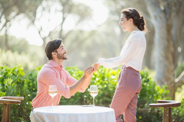 Man proposing to woman at an outdoor restaurant with engagement ring, expressing love and commitment. Ideal for use in articles and advertisements about relationships, engagements, romantic dinners, and weddings. Suitable for greeting cards, social media posts, and wedding planning brochures.
