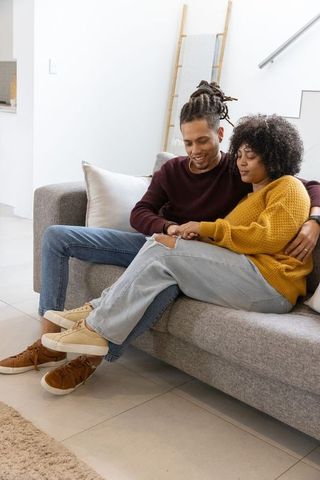 African american couple cuddling and relaxing on gray sofa in modern cozy living room