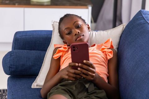 African girl reclining on blue sofa using smartphone relaxing at home digital lifestyle