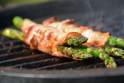 Bacon-wrapped asparagus grilling on hot grill grates with smoky char and crisp bacon