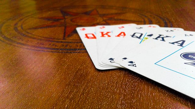 Foreground focuses on a poker hand with a royal flush on a wooden table. Background features a subtle compass design engraved into the table's surface. Useful for themes of gaming, gambling, entertainment, and leisure activities.