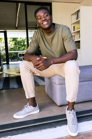 Young man sitting on ottoman in modern living room wearing olive tee and beige joggers