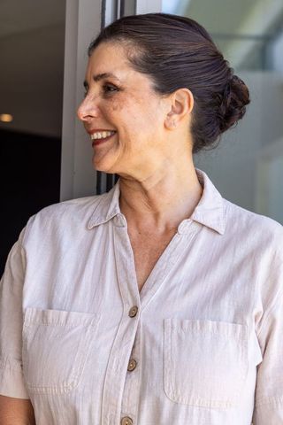 Mature woman smiling and looking left at doorway wearing beige linen button-up shirt