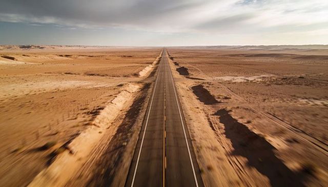 Endless straight desert highway vanishing into distant horizon over arid plains