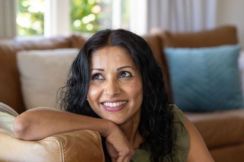 Middle-aged woman smiling and relaxing on sofa leaning on leather armrest