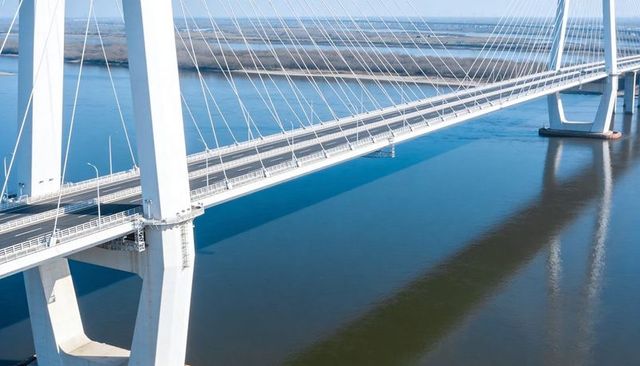 White cable-stayed bridge spanning estuary with tall pylons and glassy water reflections