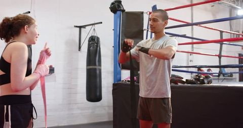 Trainer untying hand wrap while teen girl wrapping hands for sparring in boxing gym