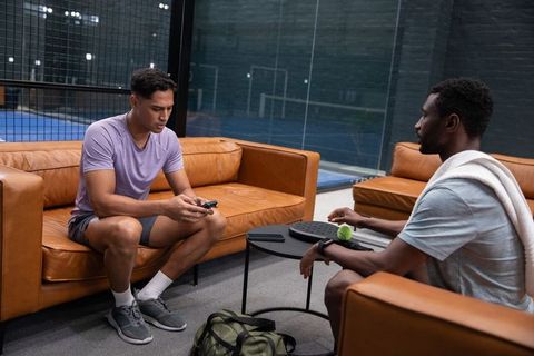 Padel teammates relaxing in lounge between matches, checking phone and preparing gear