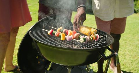 Diverse family grilling vegetable skewers in backyard celebration