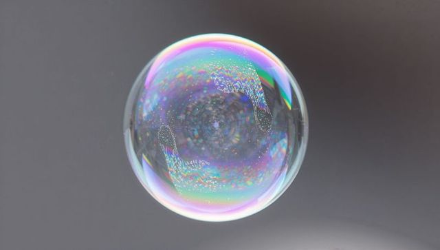 Floating iridescent soap bubble macro showing pearlescent colors against gray backdrop