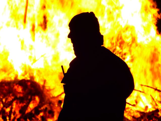 Silhouette of man standing in front of huge fire at night, conveying theme of safety and danger. Useful for illustrating fire safety, emergency scenarios, or dramatic effects in storytelling or creative presentations.