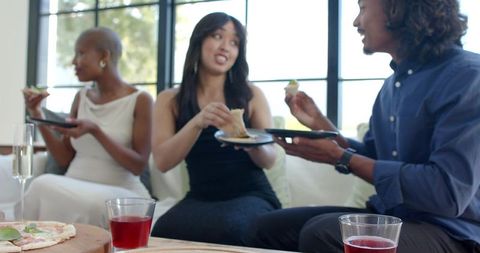 Diverse friends sharing appetizers and drinks on sofa during relaxed home gathering