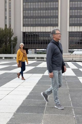Senior man walking on checkerboard plaza with woman in background urban walking lifestyle