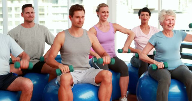 Fitness group sitting on exercise balls lifting hand weights at the gym