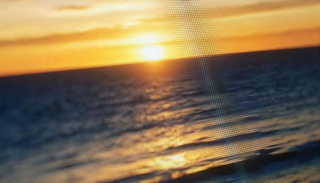 Sunset through mesh screen casting golden reflections across ocean horizon