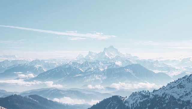 Snow-covered alpine peak rising above layered ridges and misty valleys, panoramic