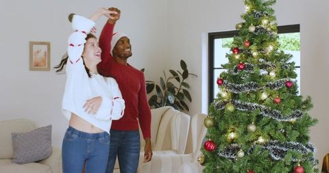 Diverse Couple Joyfully Dancing Near Christmas Tree at Home
