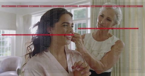 Senior caregiver placing earring on woman in satin robe in sunlit room with hud