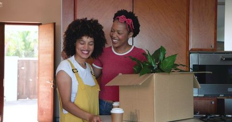 Happy Women Unpacking Box in Modern Kitchen of New Home