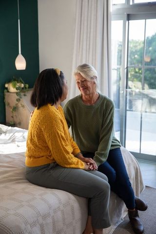 Sunlit bedside support: mature woman comforting friend, holding hands, intimate connection