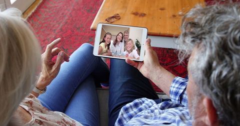 Senior couple video chatting with family online from home couch